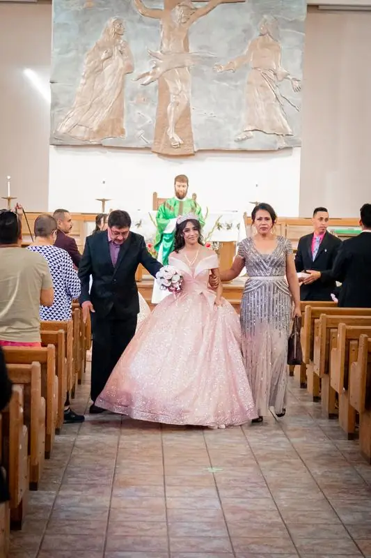 Young woman in a pink gown walking down a church aisle