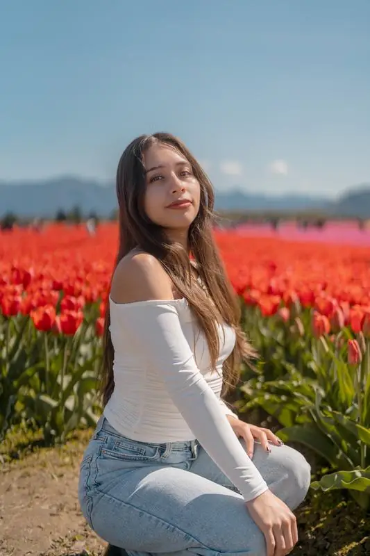 Woman sitting in a field of red tulips with mountains behind